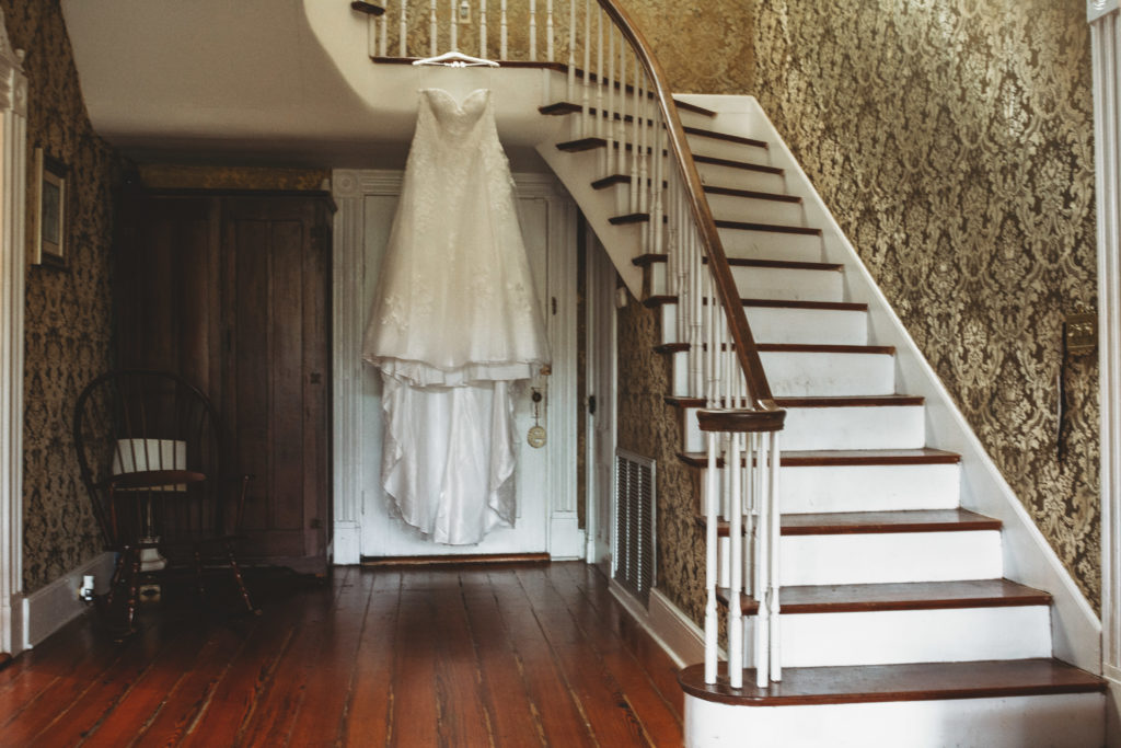 Bride's wedding dress hanging on the banister of the stair rail at Englund Estate Venue in Georgia. 