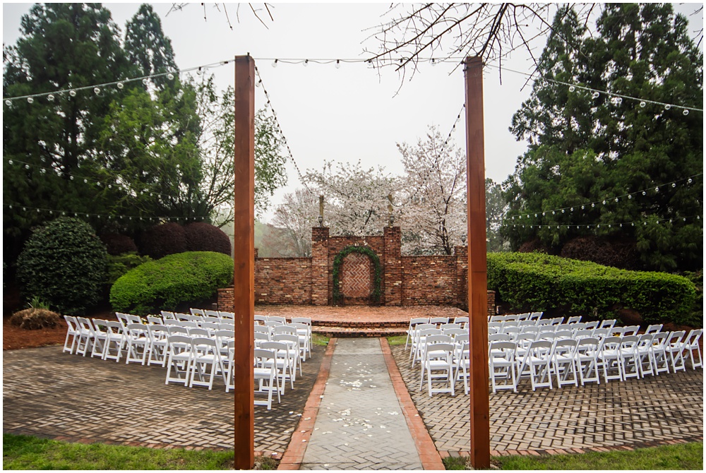 the carl house wedding venue in auburn georgia has a brick ceremony site with a brick wall, fold out chairs for seating and strung lights 