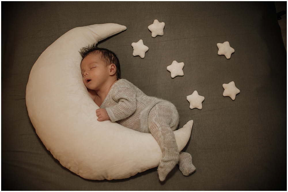 Flowery Branch photographer takes photo of the baby with props during the newborn session in the studio. Baby is laying in between the moon and stars.